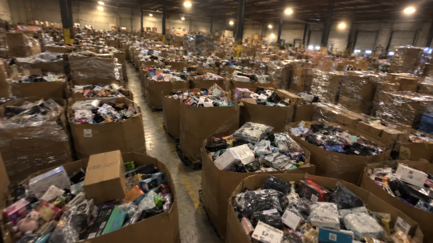 Busy warehouse floor packed with large bins overflowing with mixed returned merchandise